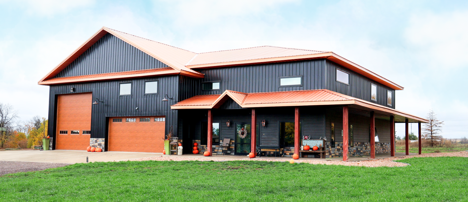 Reaves Buildings Barndominium with a covered porch, horizontal rectangle windows, an oversized garage door and 2 car garage door with dark gray siding and rust-colored roof and accents.